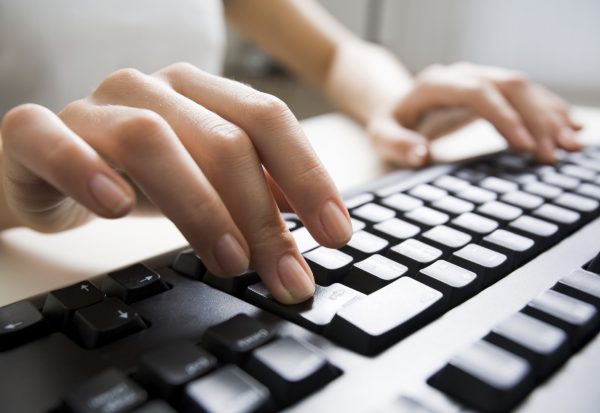 Close-up of female hands touching buttons of black computer keyboard